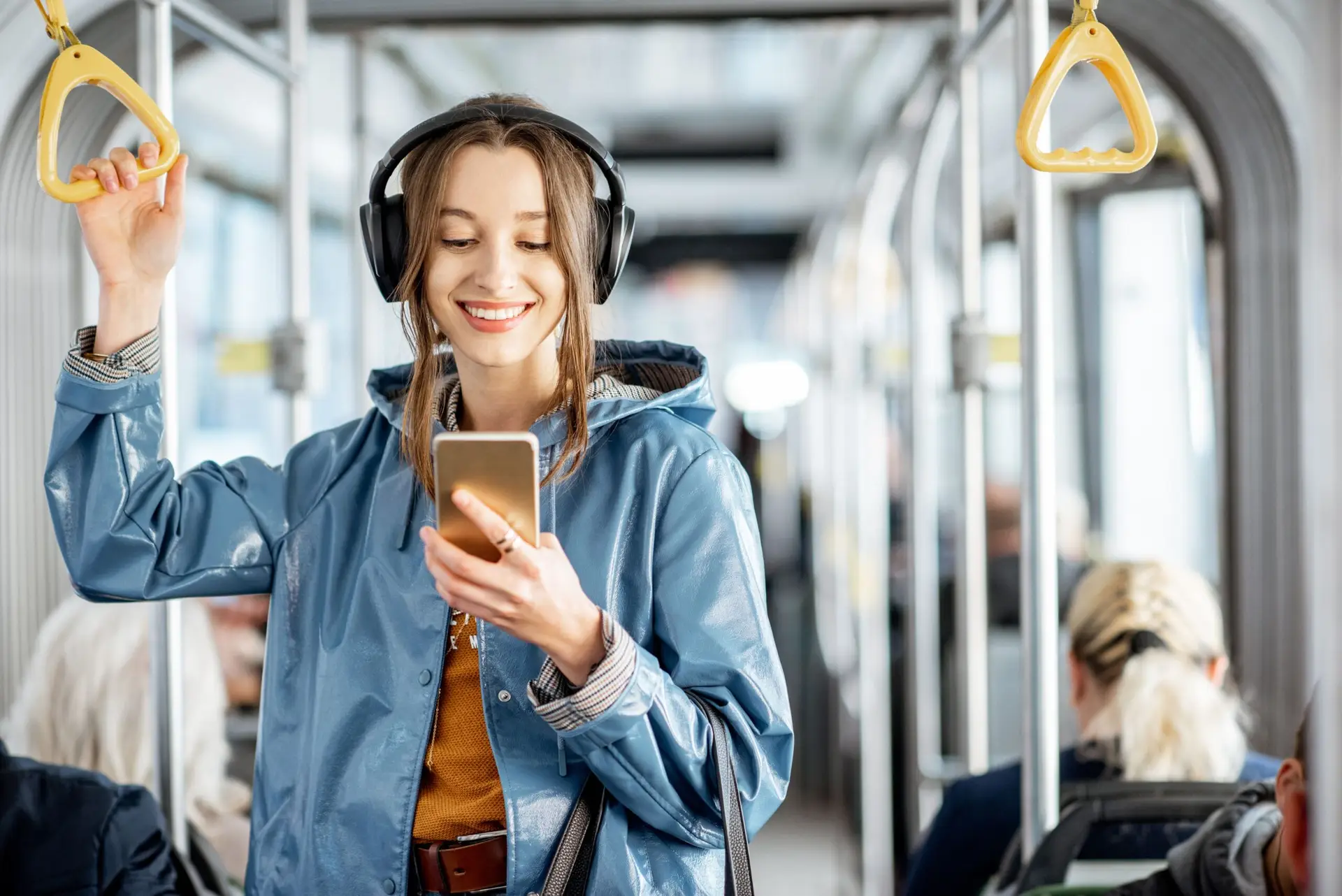 Jonge vrouw passagier staande met koptelefoon en smartphone tijdens het bewegen in de moderne tram, genieten van een reis in het openbaar vervoer